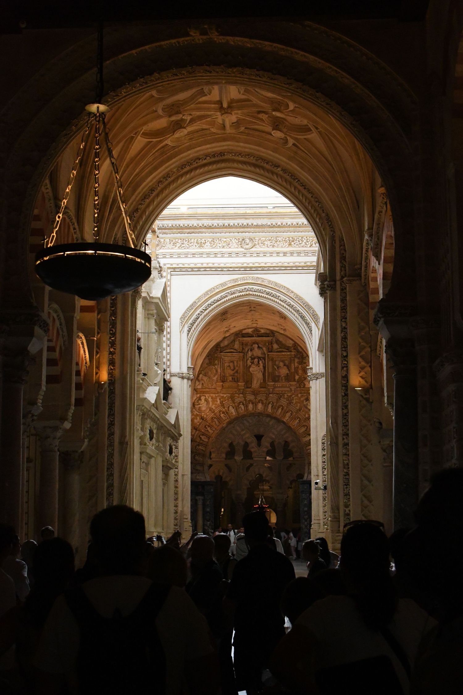 Interior view of a cathedral with arched doorways and hanging chandelier in dim lighting.