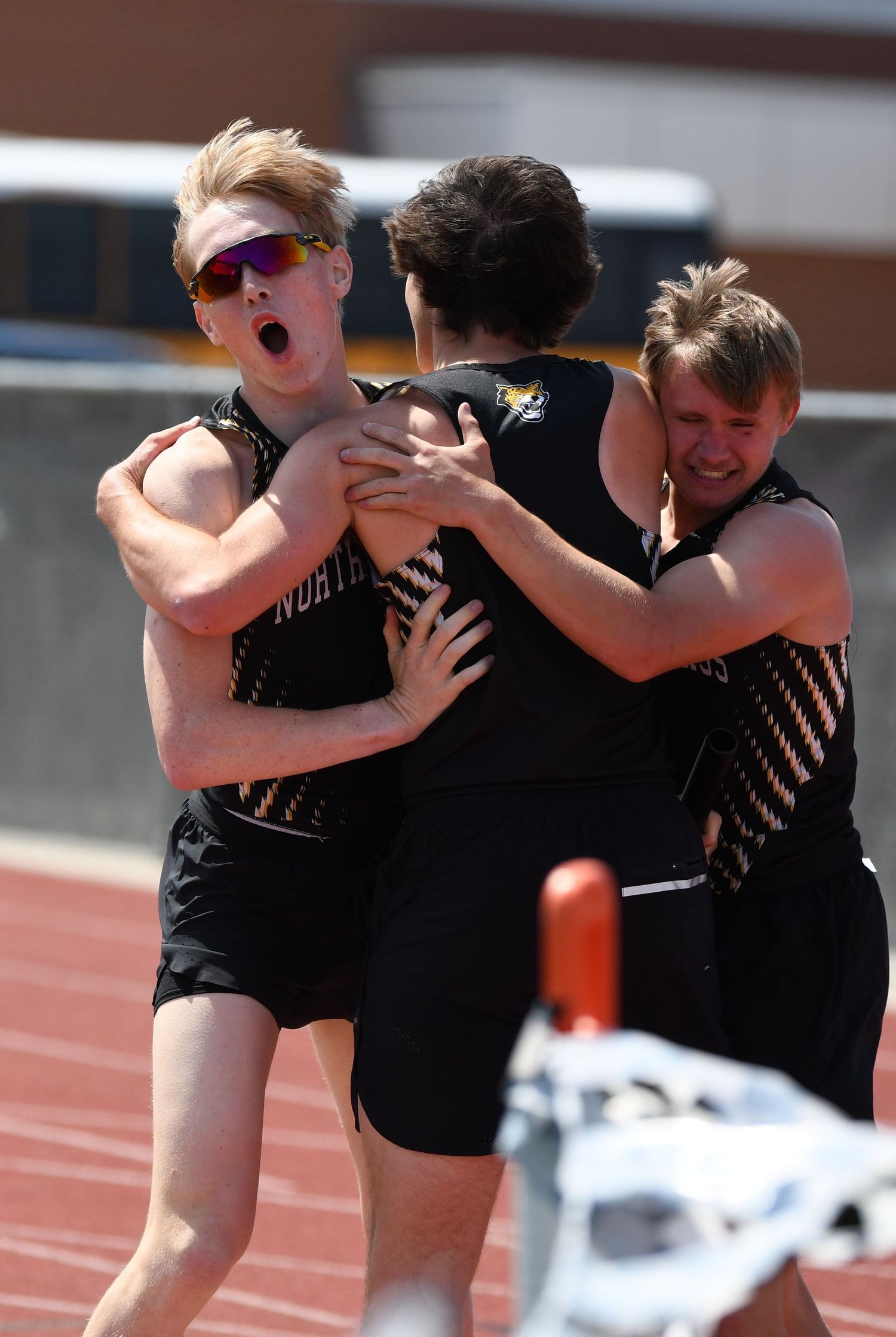 Athletes in black uniforms celebrate together on track field during competition.