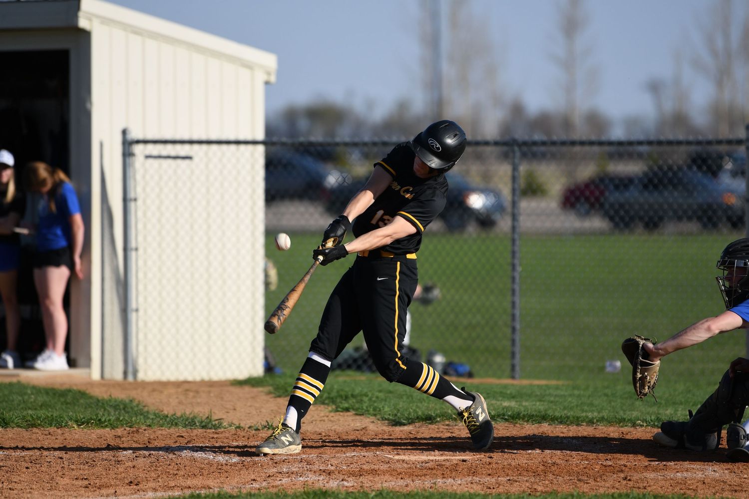 Baseball player in black and gold uniform swings bat during game.