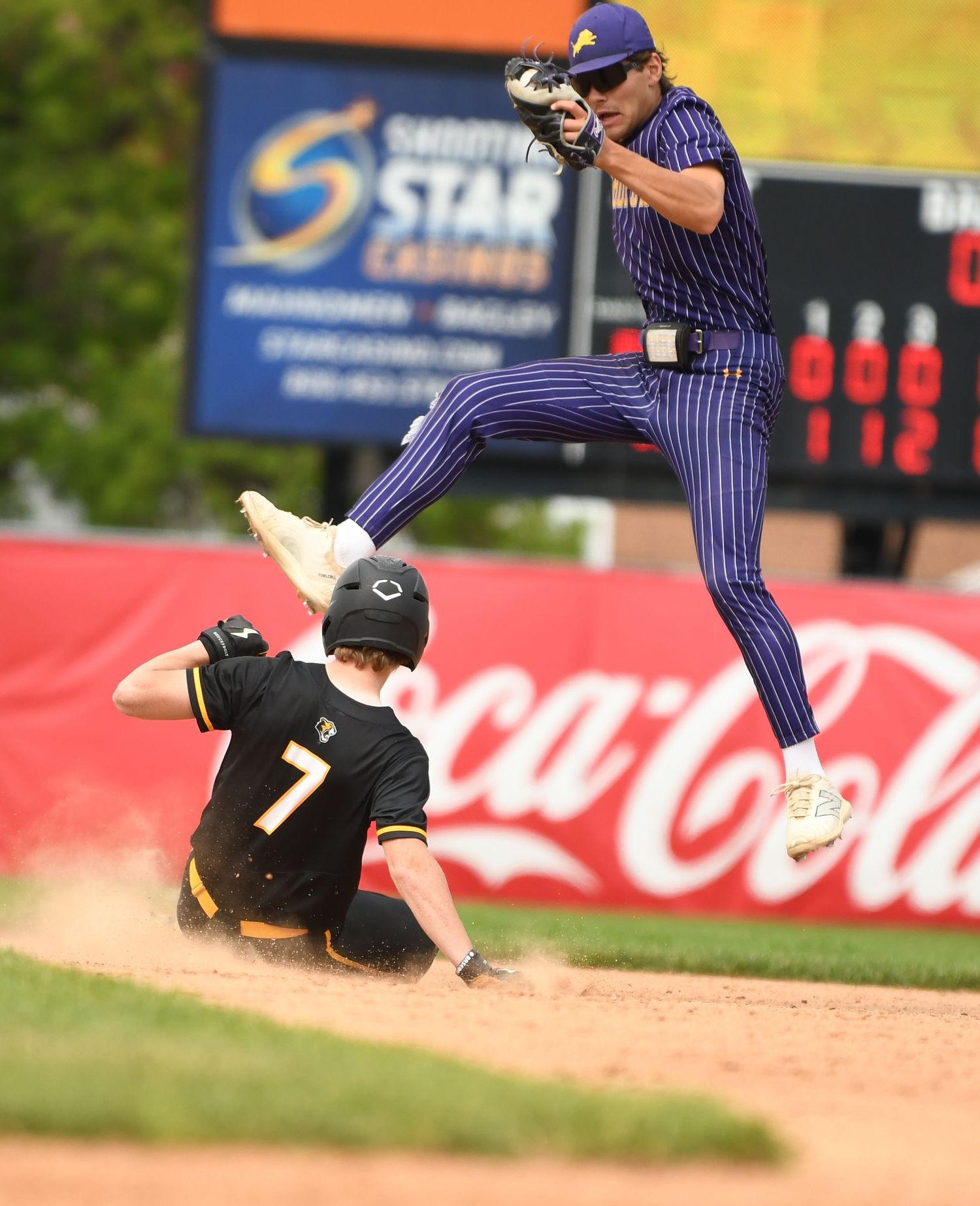 Baseball play shows dramatic sliding action at second base with player jumping to avoid collision.
