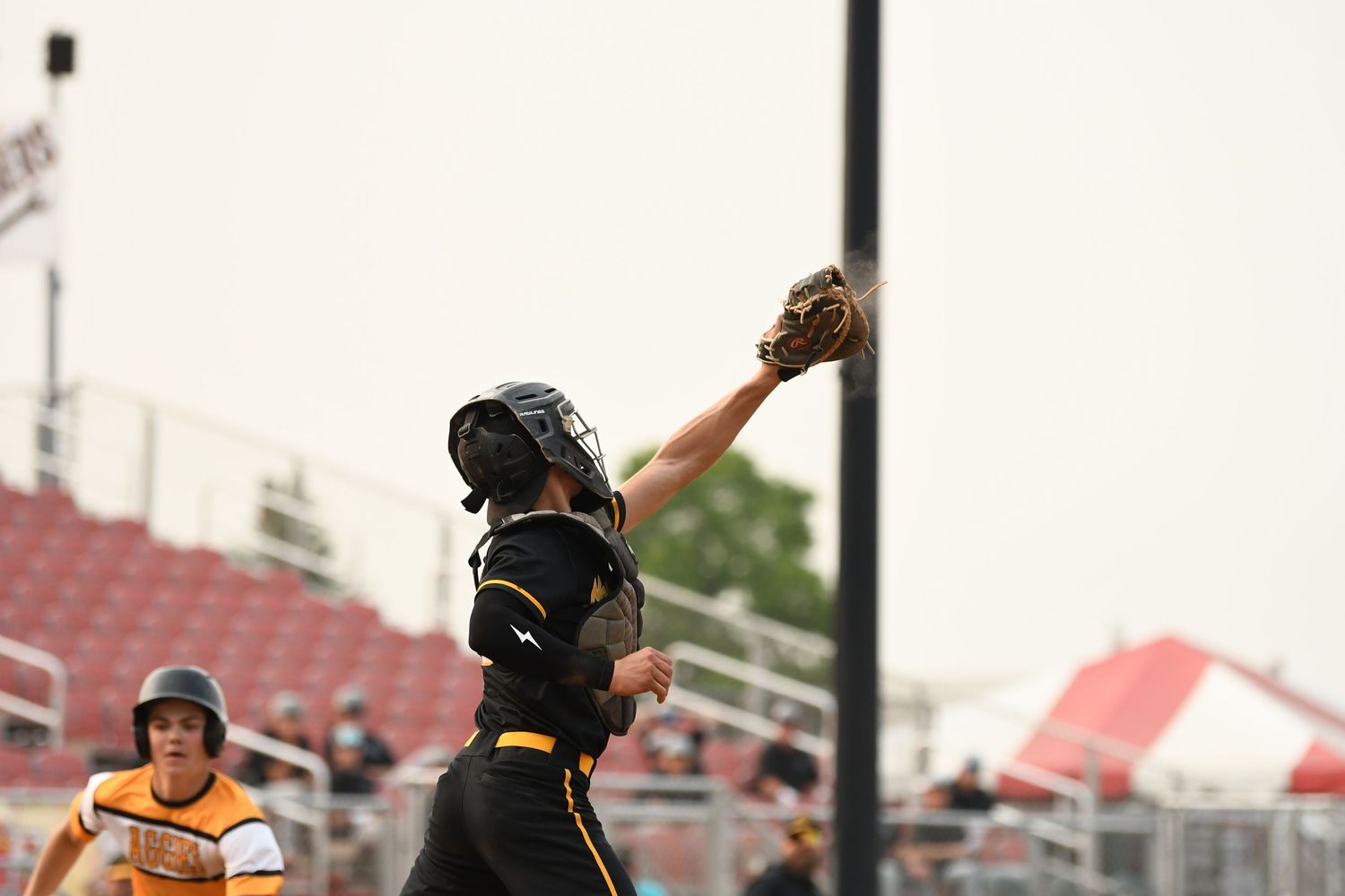 Baseball player reaches high to catch ball against stadium backdrop.