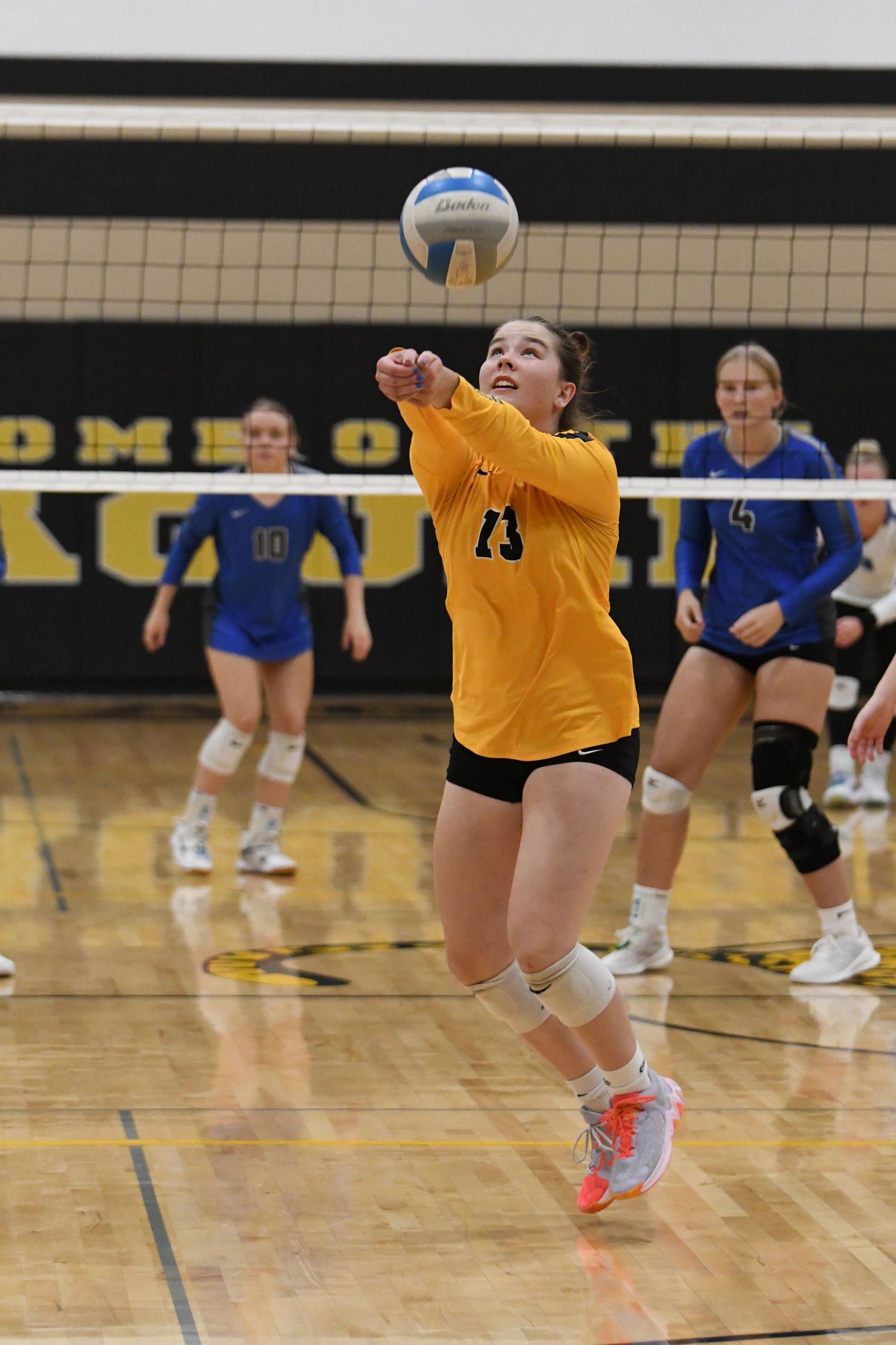 Volleyball player in a yellow jersey dives to save a ball during an intense match on a wooden court.