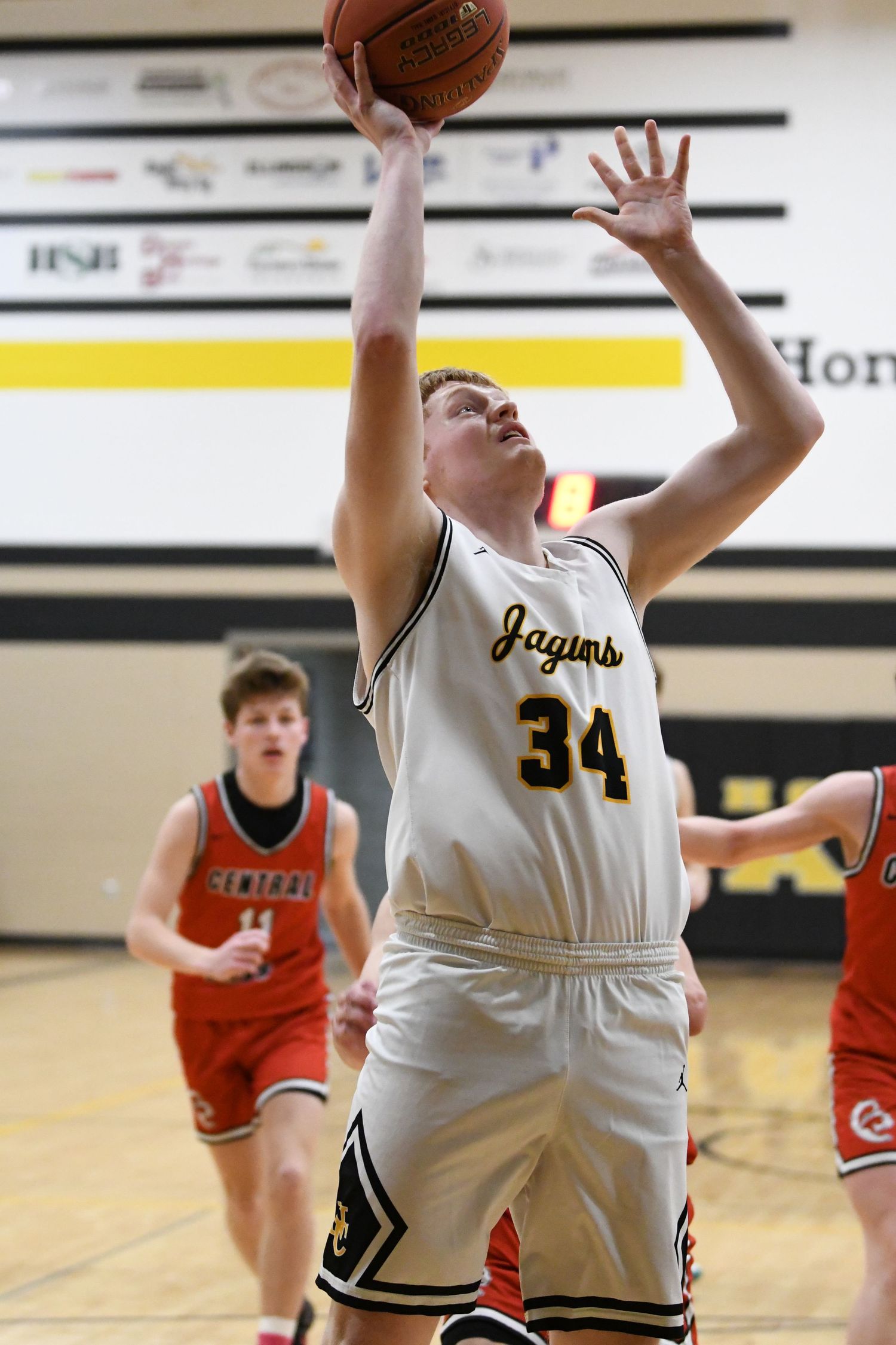 Basketball player in white jersey reaches up for rebound during game.