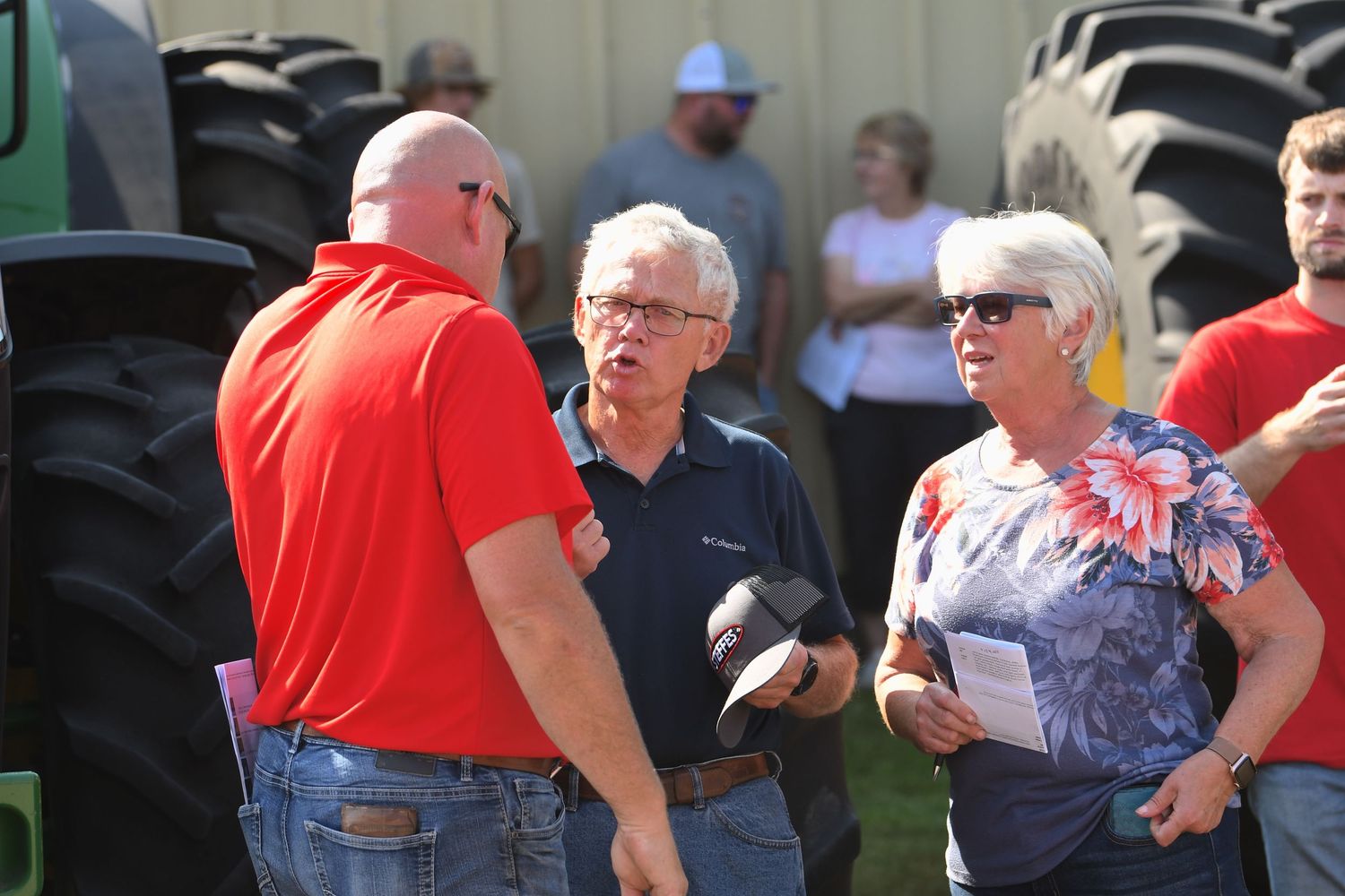 Group of spectators sitting and standing at an outdoor event wearing casual attire and red shirts.