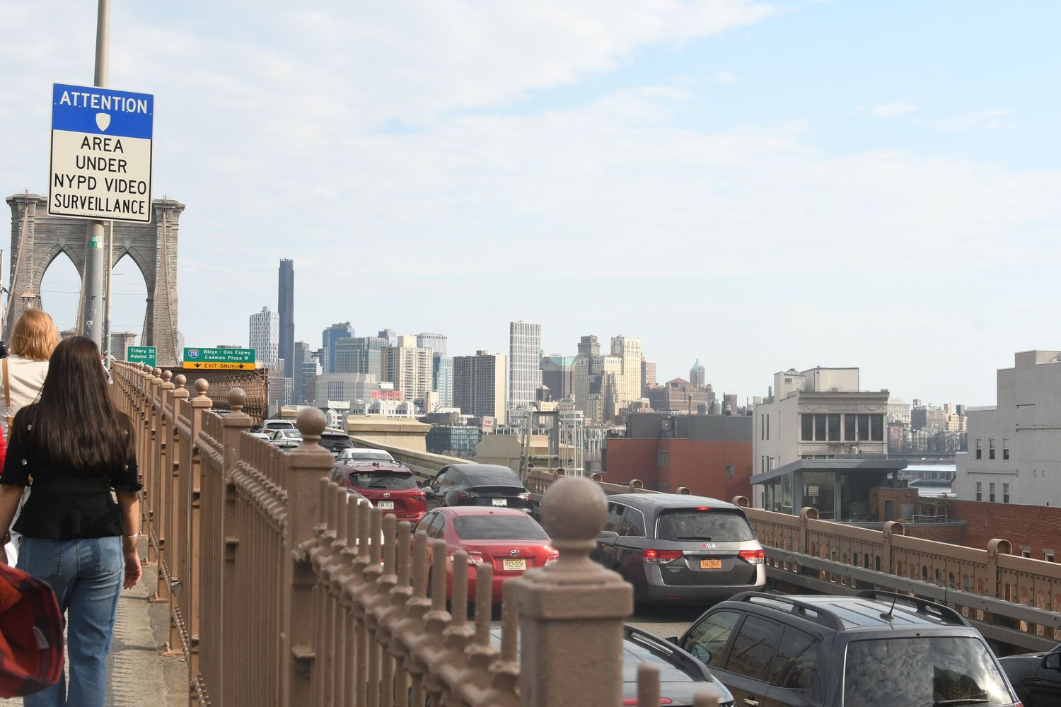 Brooklyn Bridge walkway with traffic and Manhattan skyline view on a sunny day.