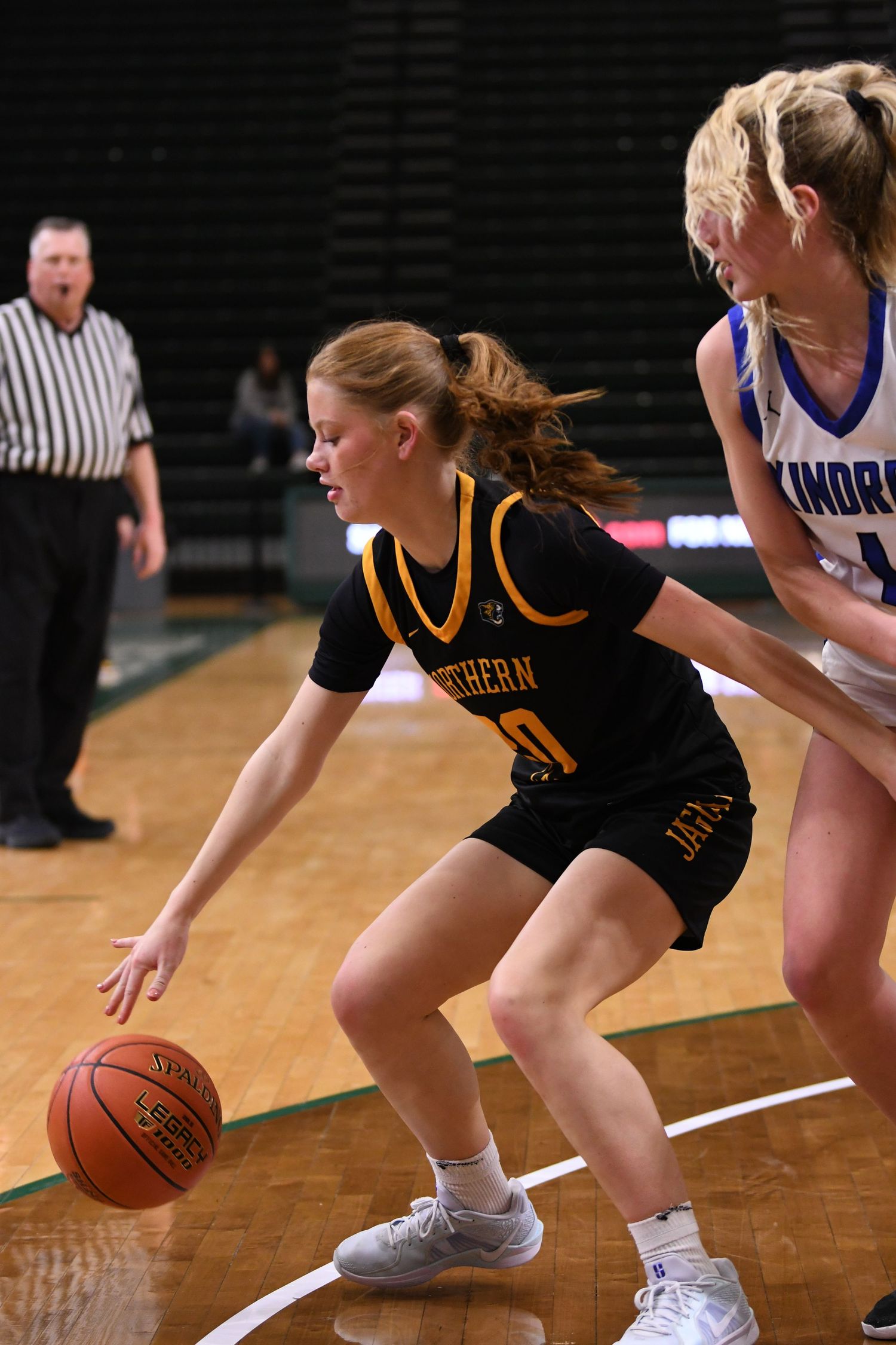 Basketball player in black uniform dribbles while being defended during game.