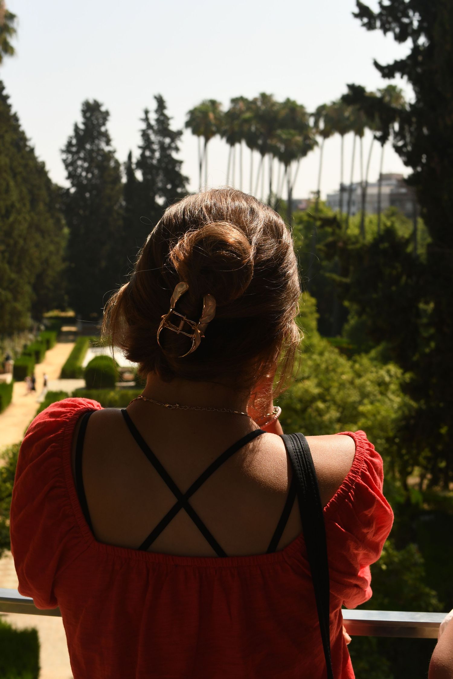 Back view of someone in a red top looking out over a scenic garden landscape.