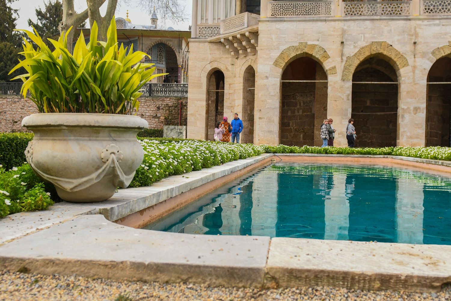Historic Mediterranean courtyard with ornate stone architecture and tranquil swimming pool surrounded by lush gardens.