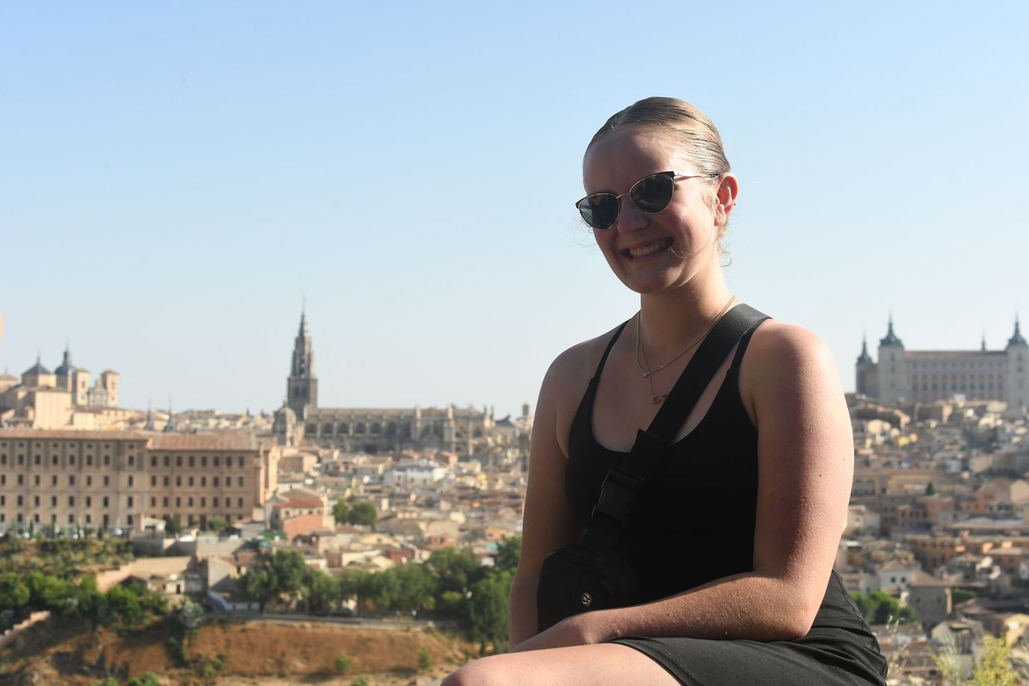 Tourist overlooking historic Toledo cityscape with cathedral spires visible in background.