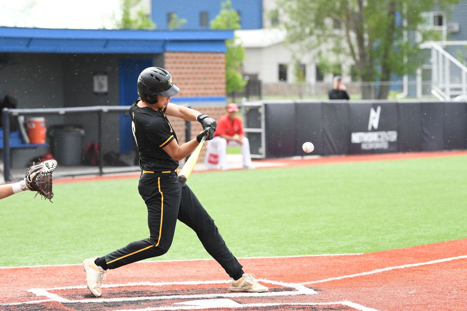 Baseball player in black and gold uniform swings the bat at home plate.