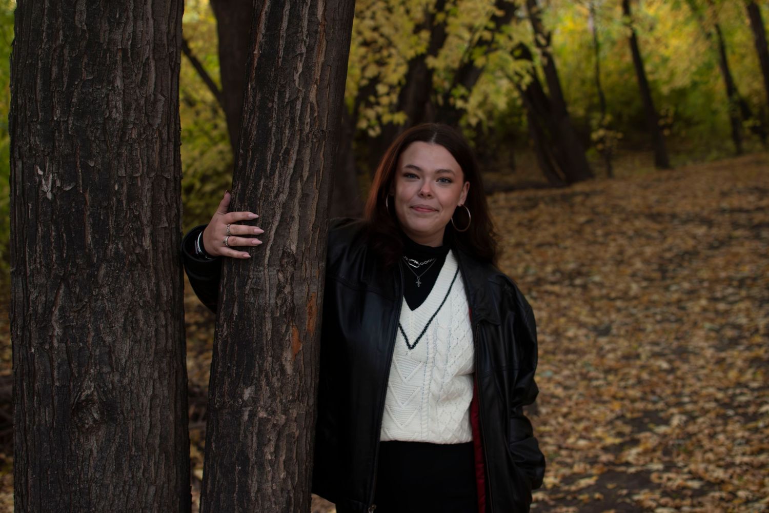 A couple embraces in a romantic autumn forest setting surrounded by fallen leaves and tall trees.