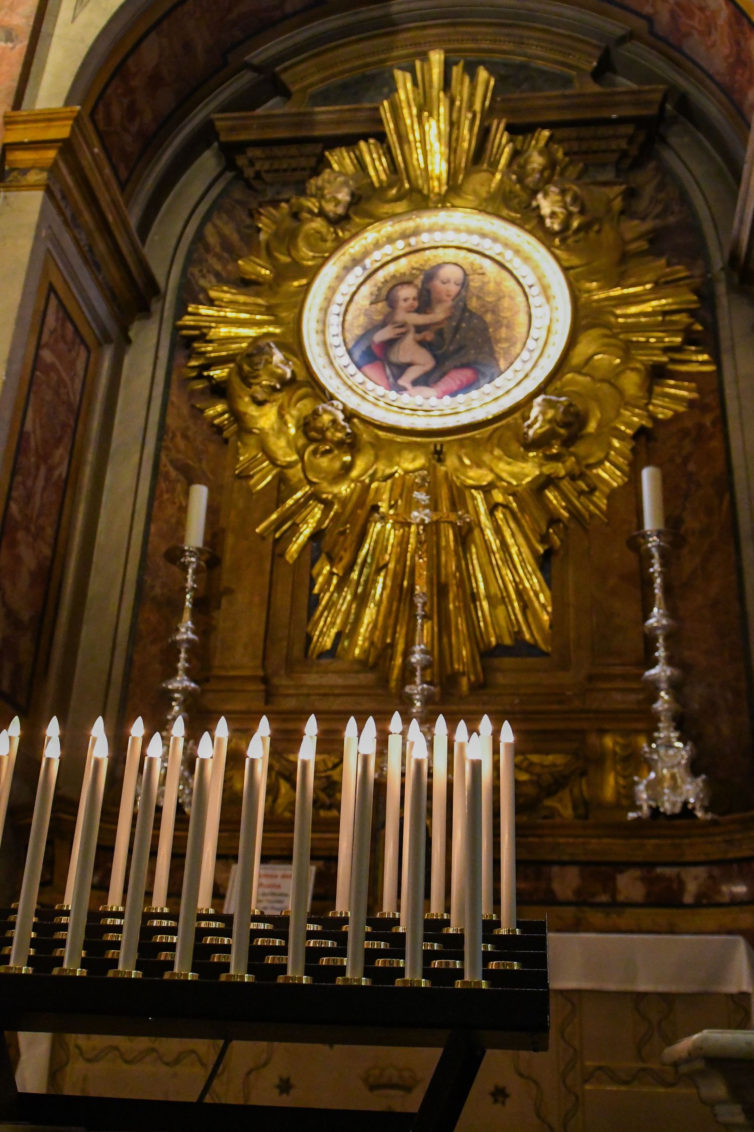 Gilded church altar with white candelabras and religious artwork in circular medallion.