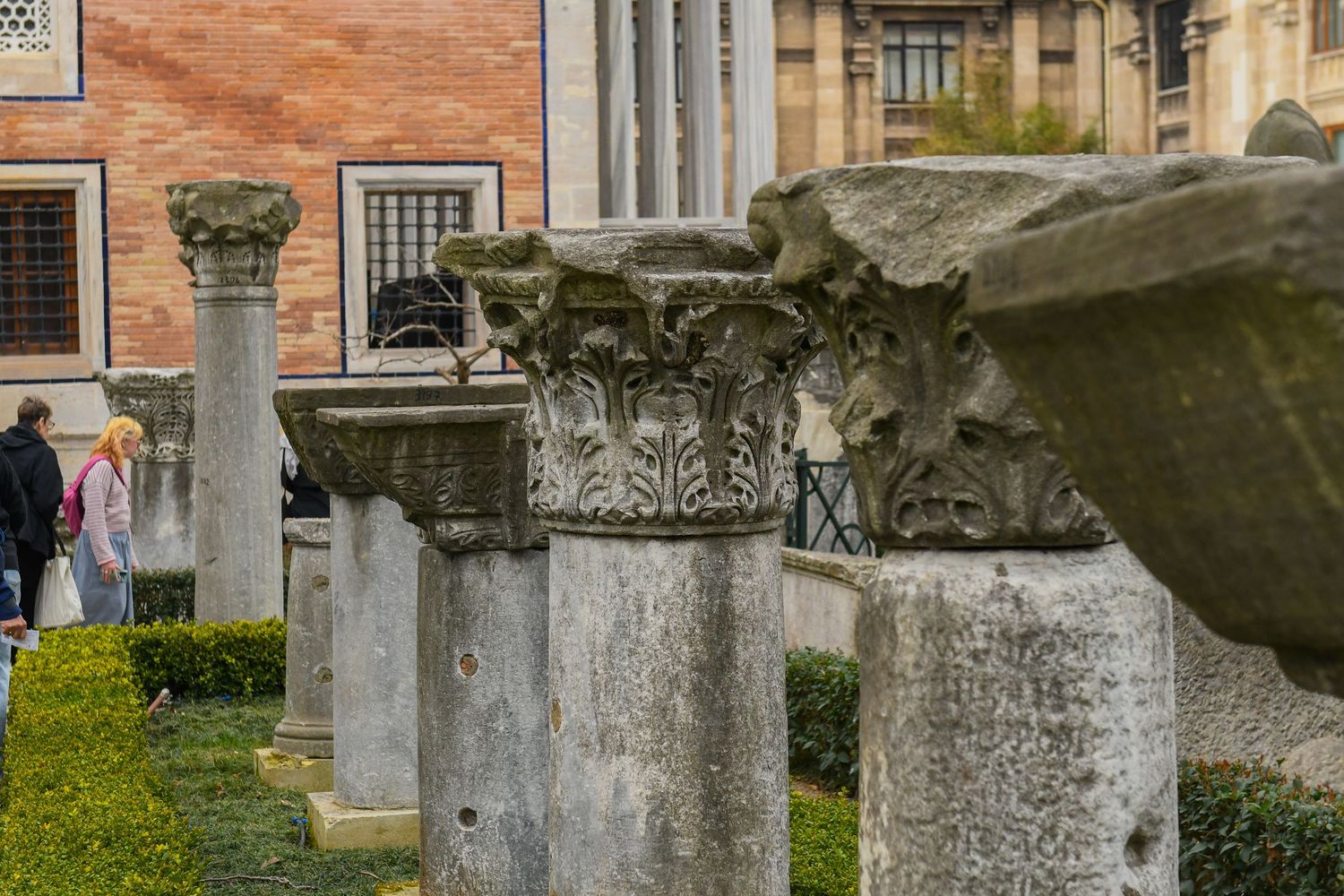 Row of weathered stone columns and architectural ruins against a brick building.