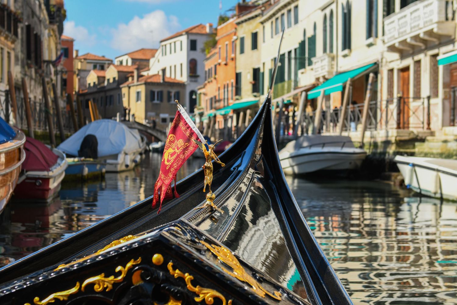 Ornate gondola bow on a scenic Venice canal with colorful buildings and boats in the background.