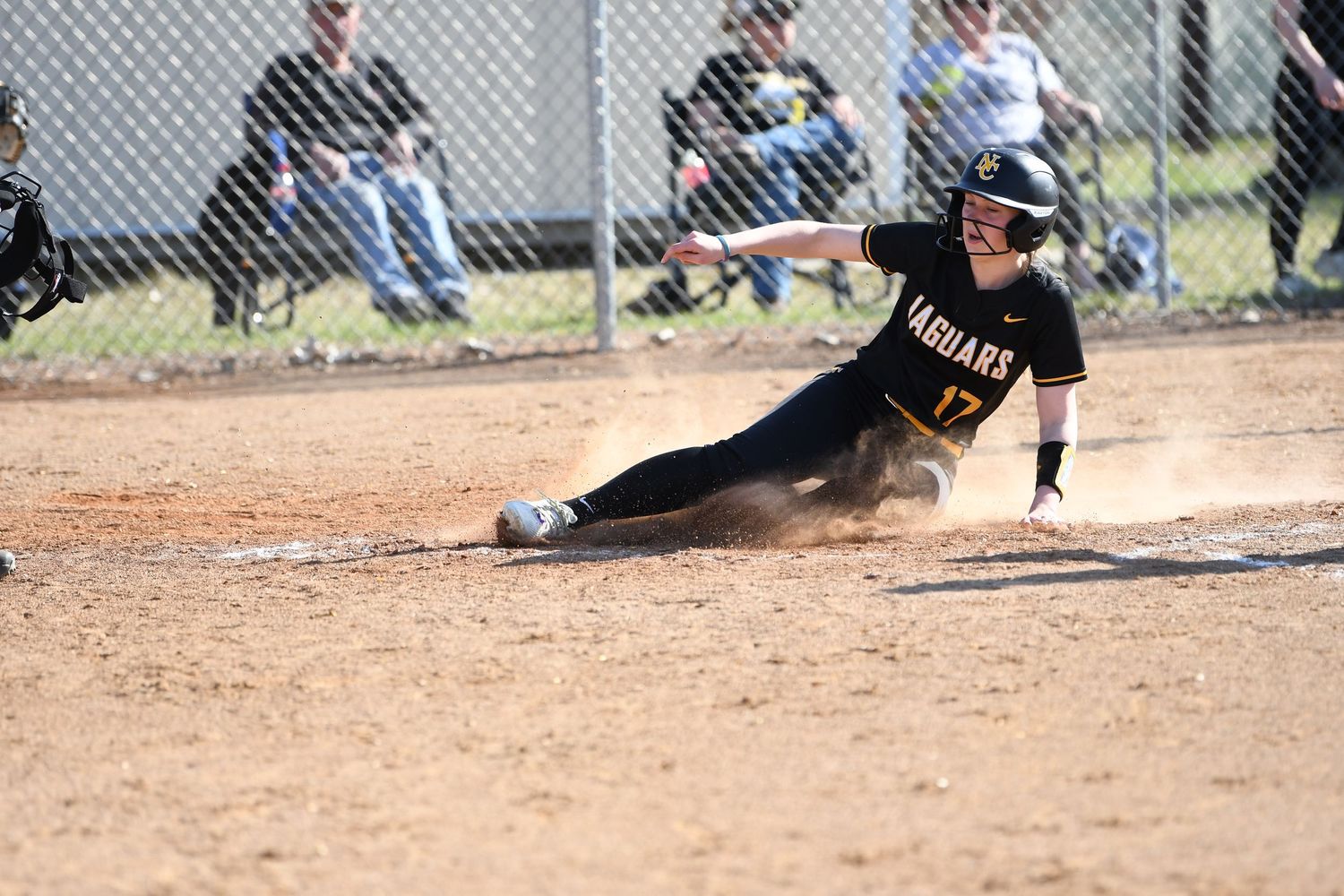 Player sliding into base during competitive softball game on dirt field.