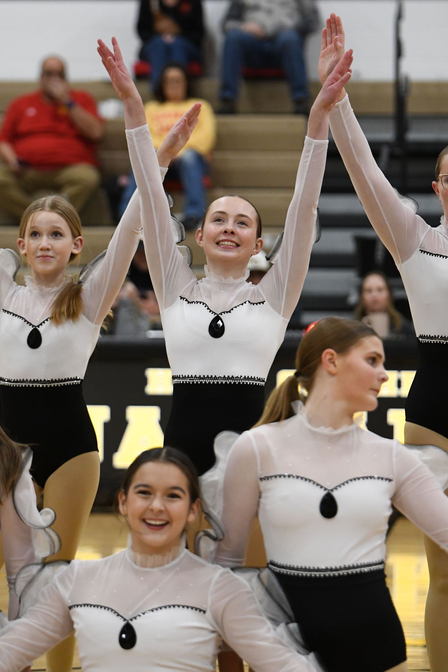 Dance team performs synchronized routine wearing matching black and white costumes in gymnasium.