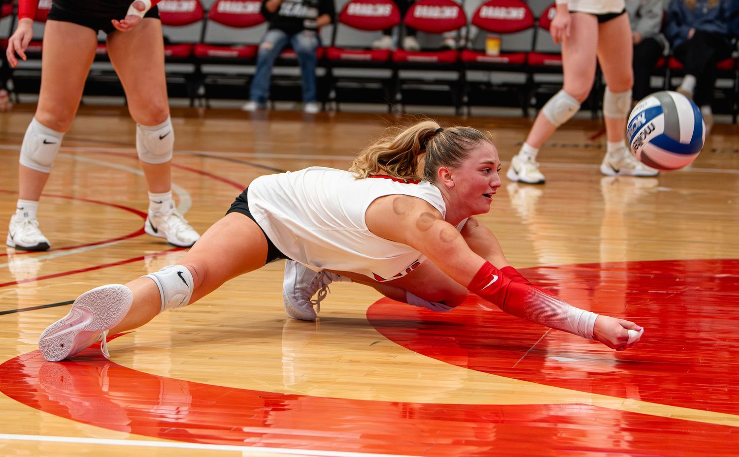 Volleyball player dives for the ball on a red court during an intense match.