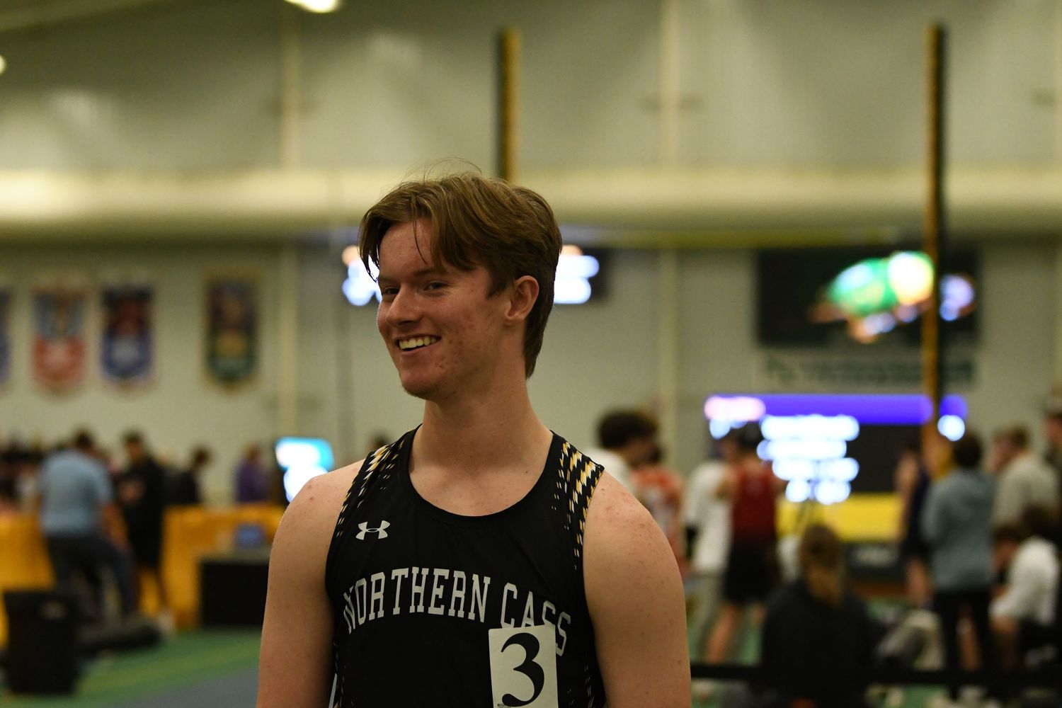 Athletes warm up and compete at an indoor track and field meet facility.