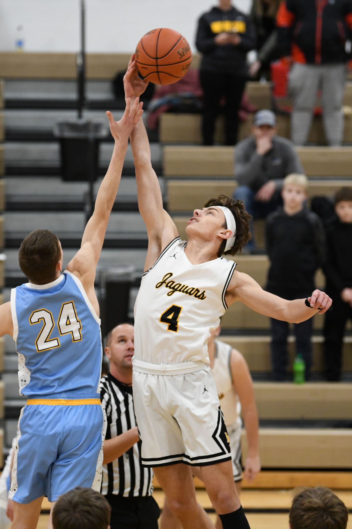 Basketball players jump for the tip-off as referee holds ball at center court.