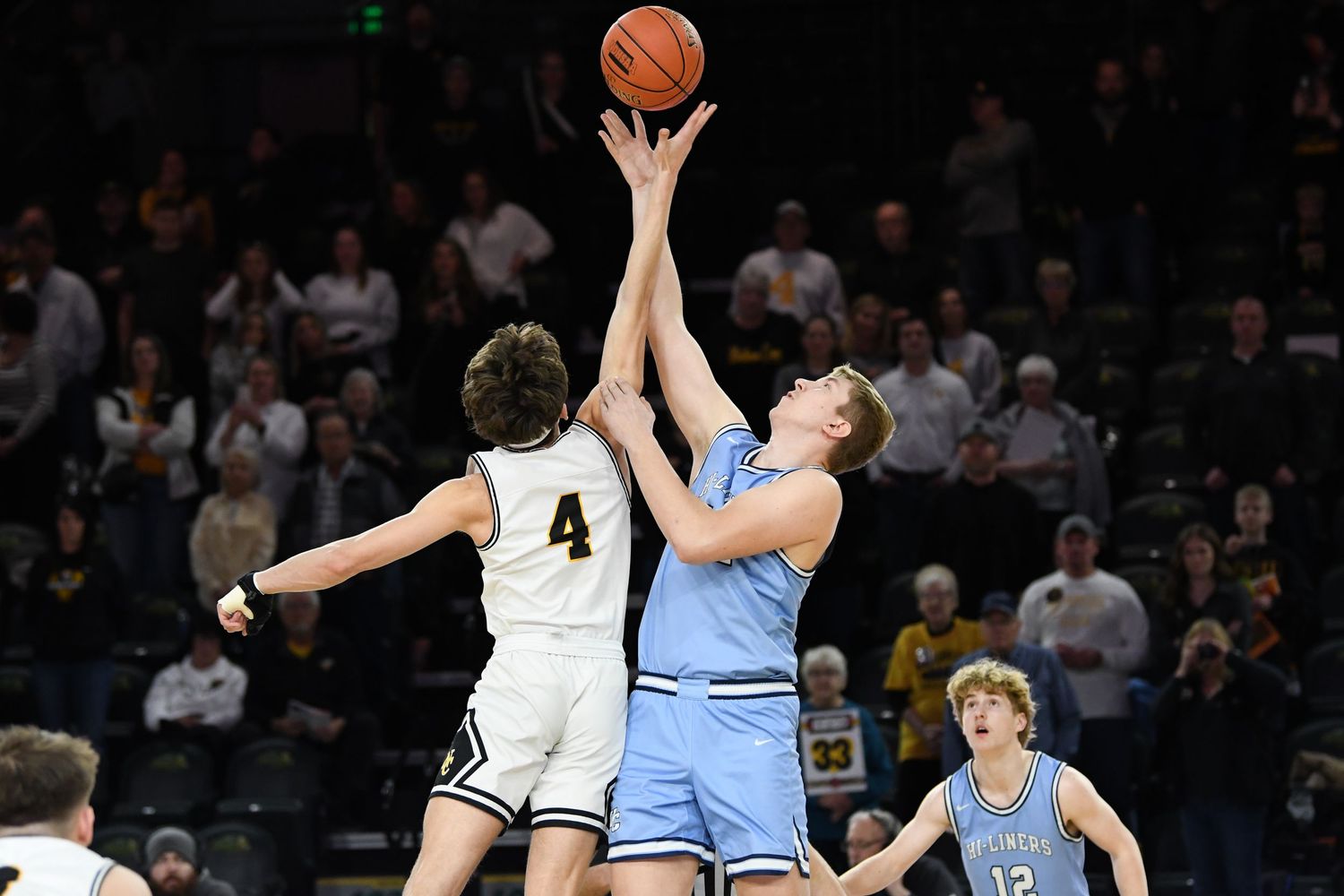 Two basketball players jump high to compete for possession of the ball during an intense game.