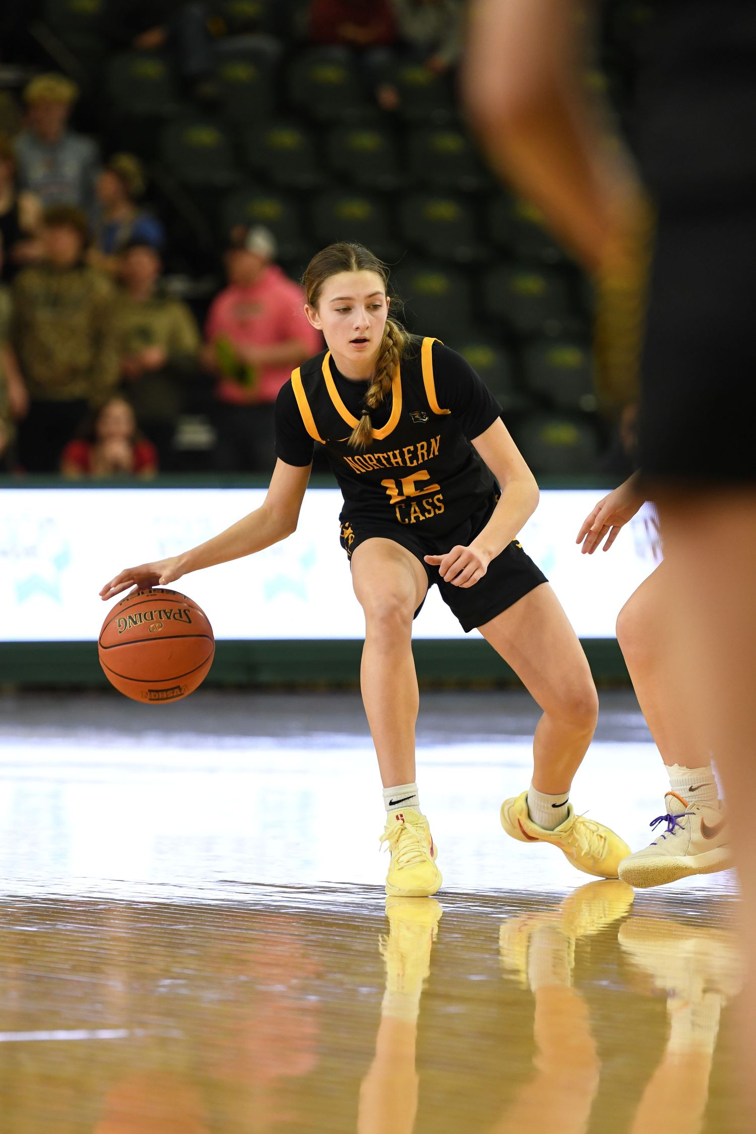 Basketball player in black and gold uniform controls the ball at the top of the key.