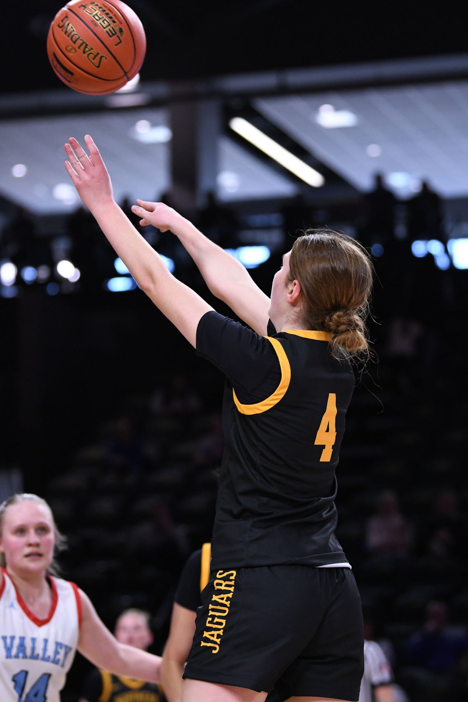 Basketball player in black uniform attempts jump shot on court.