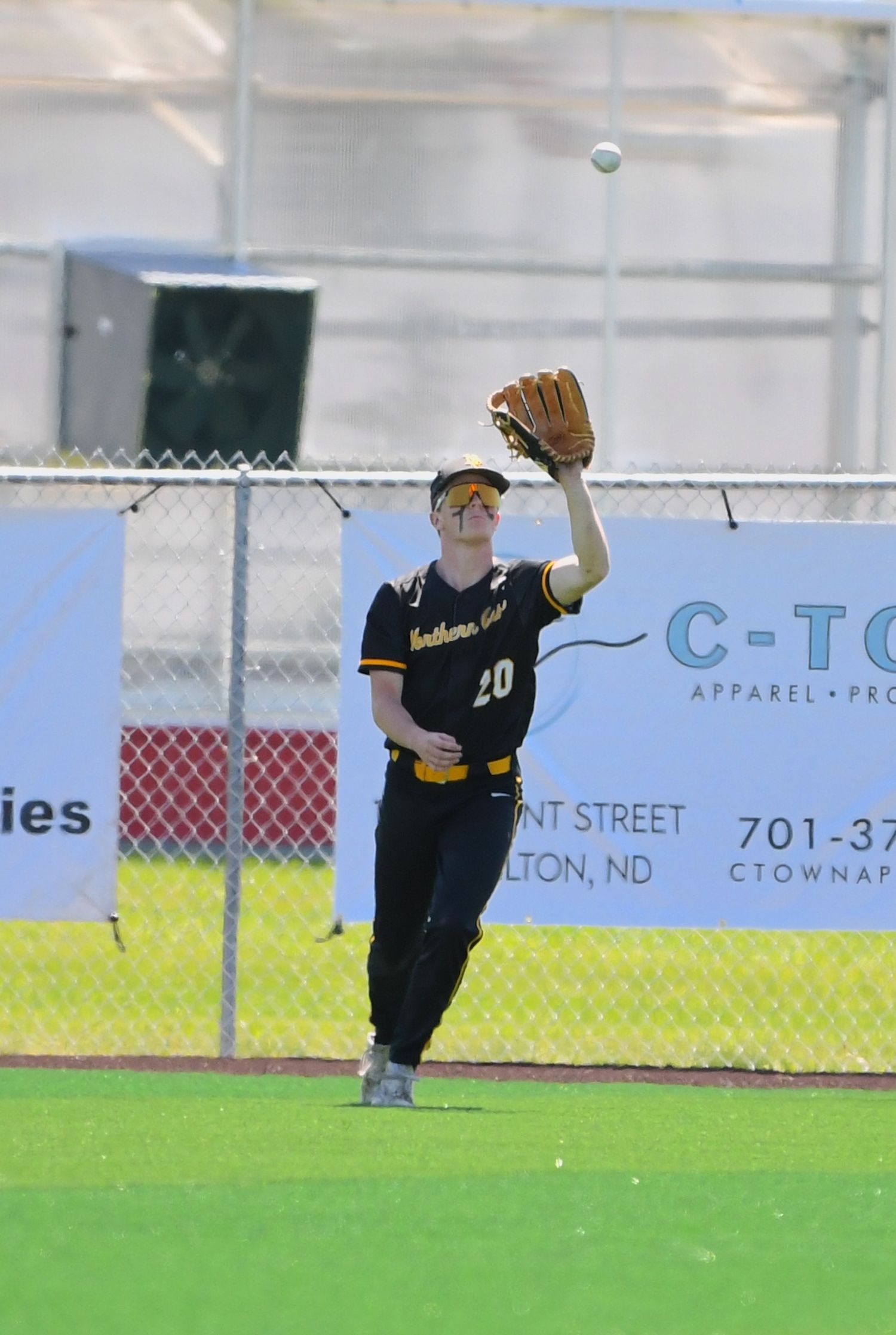 Outfielder in black jersey reaches up to make a catch against the fence.