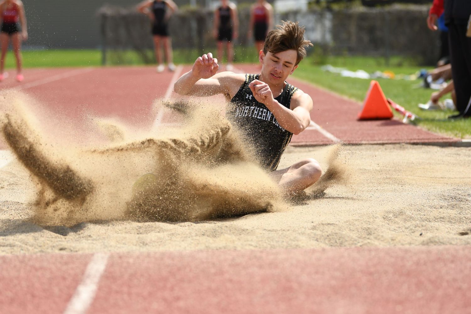 Sand sprays as athlete completes landing during long jump competition.