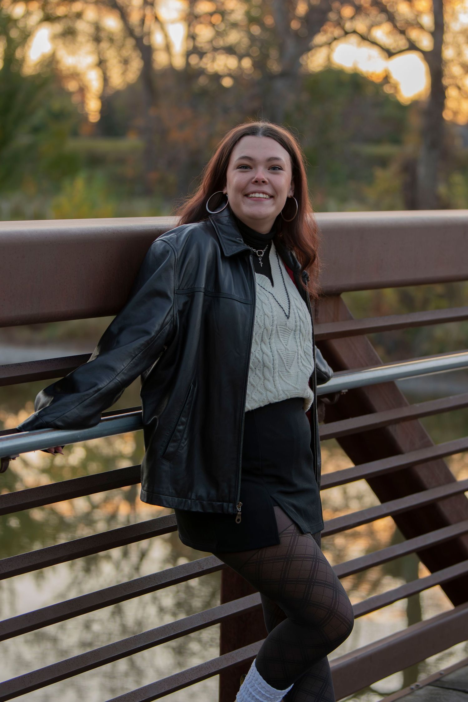 Person in leather jacket poses playfully on wooden railing during golden hour sunset.