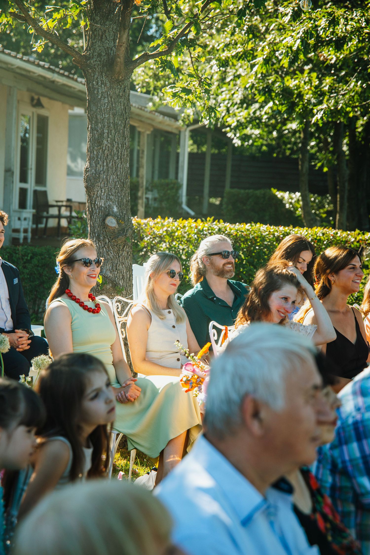 Wedding guests seated outdoors in a sunlit garden enjoying a summer ceremony celebration.