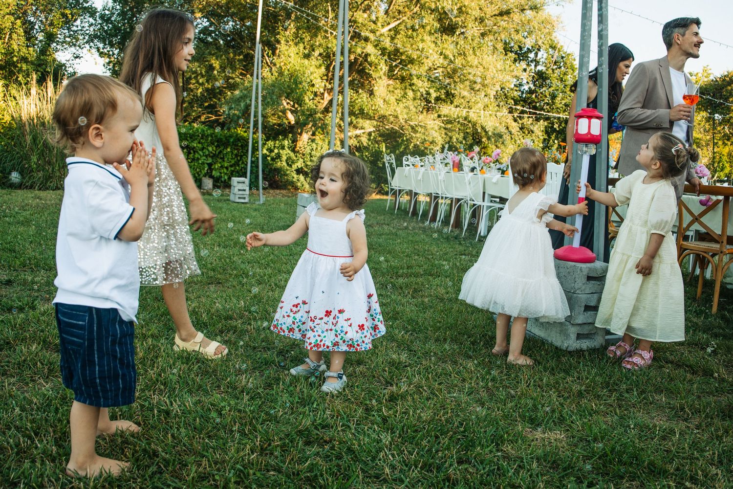 Children in formal attire playing on green grass at an outdoor wedding ceremony on a sunny day.