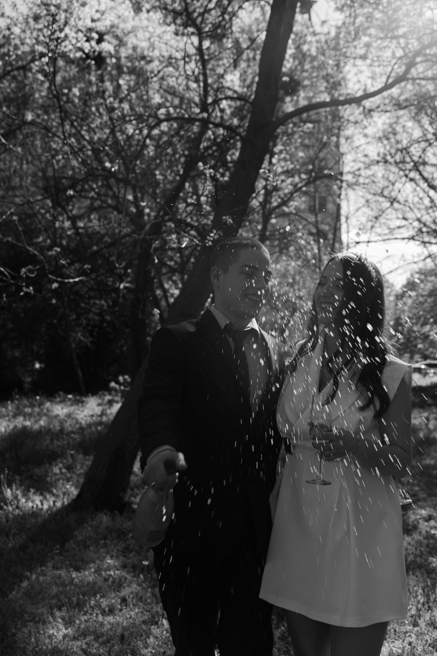 Black and white photo of bride and groom walking through forest with confetti falling.