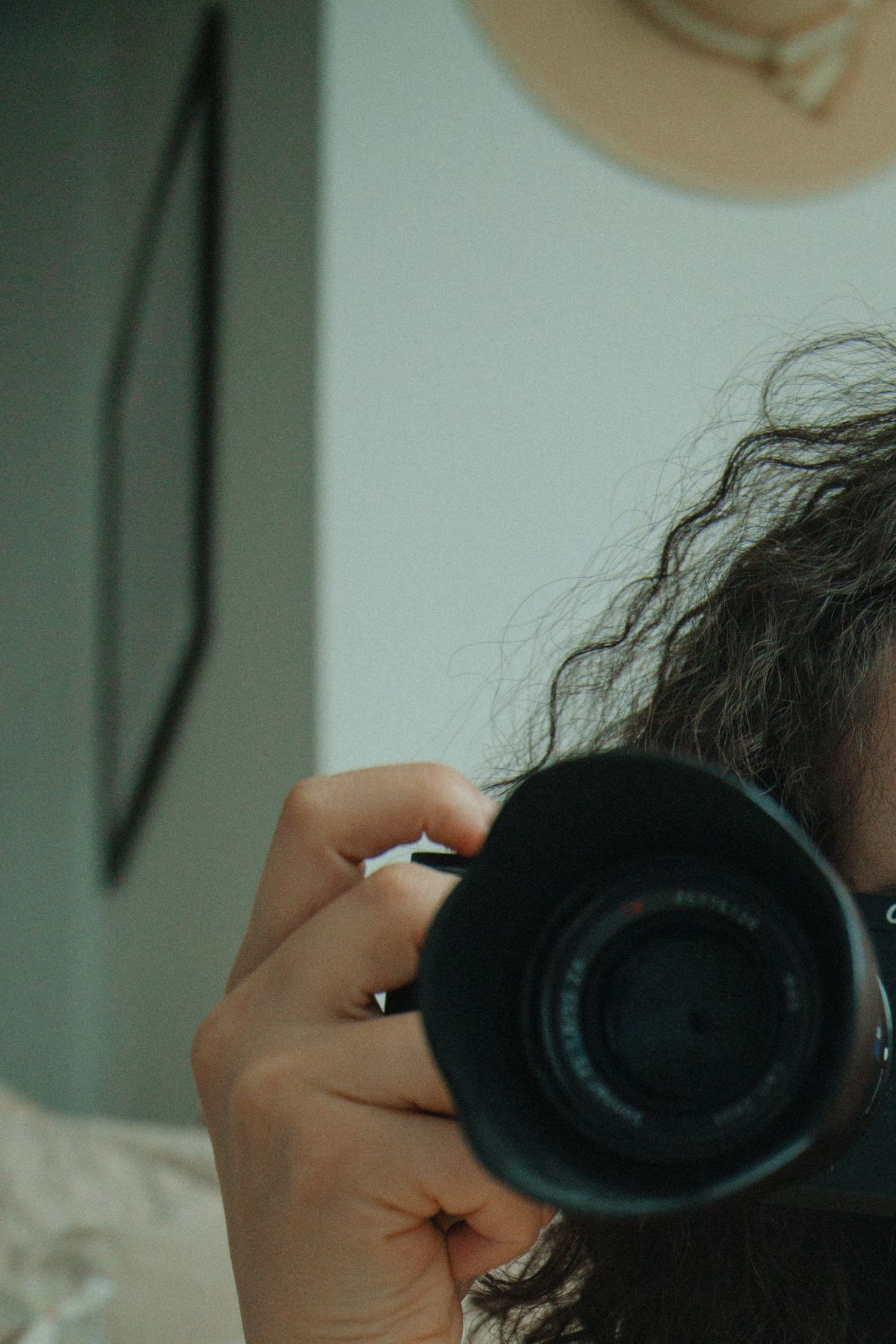 A person holds a camera lens close to their face while taking a photograph in a dimly lit setting.