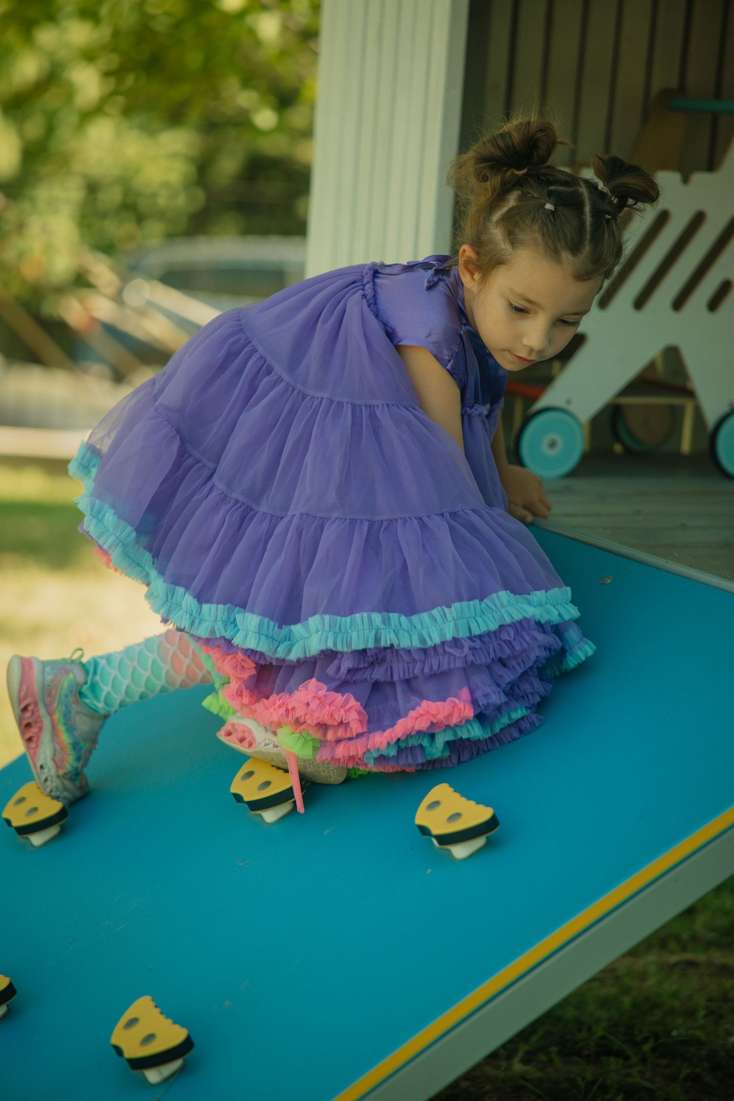 Young girl in purple tutu dress playing on blue playground equipment outdoors.