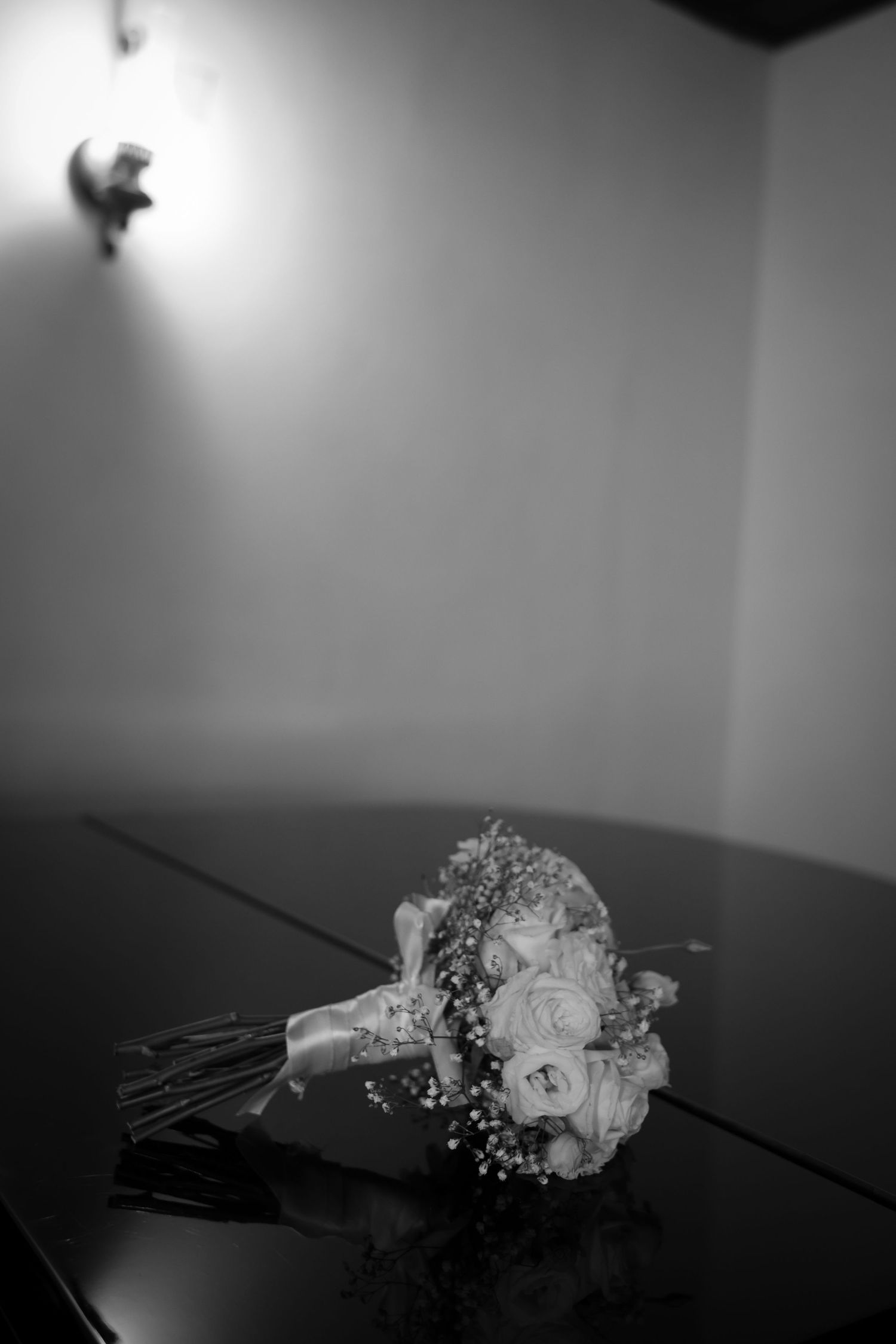 Black and white photo of a bridal bouquet with roses and baby's breath resting on a reflective dark table.