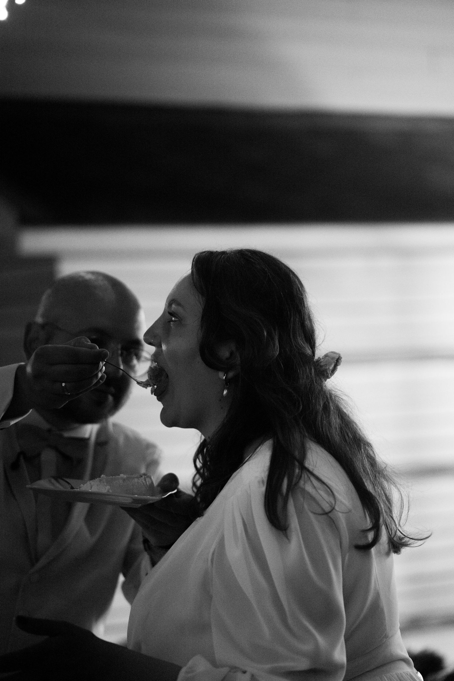 Black and white candid of woman being fed wedding cake at elegant reception celebration.