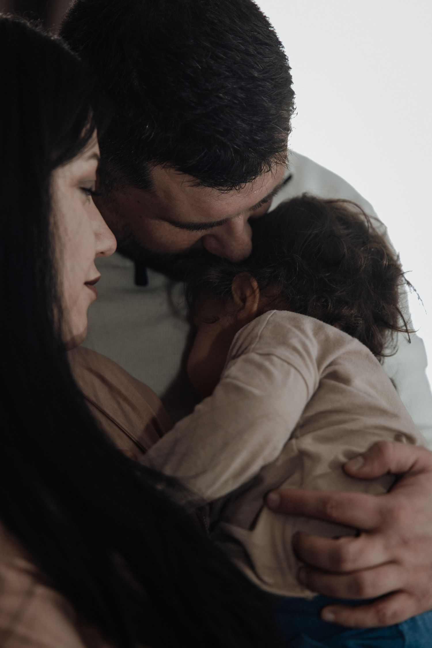 A tender family moment as a father kisses his baby while the mother lovingly holds the child close.