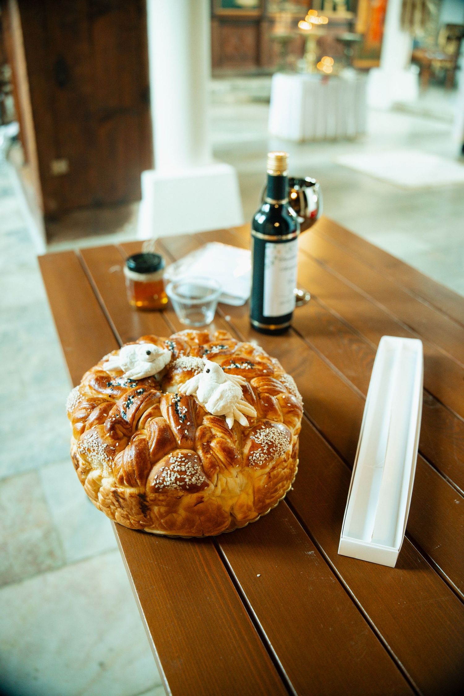 Traditional decorated braided bread loaf on wooden table with wine bottle and glasses in restaurant setting.
