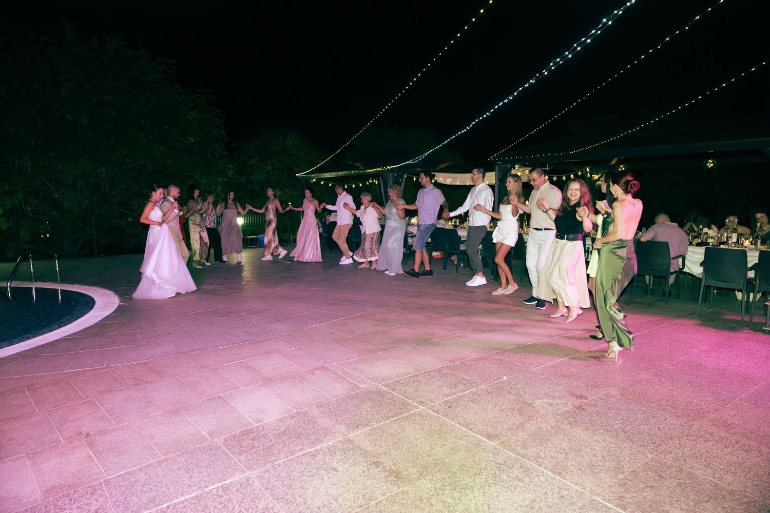 Guests dancing on illuminated outdoor dance floor with string lights at elegant evening wedding reception.