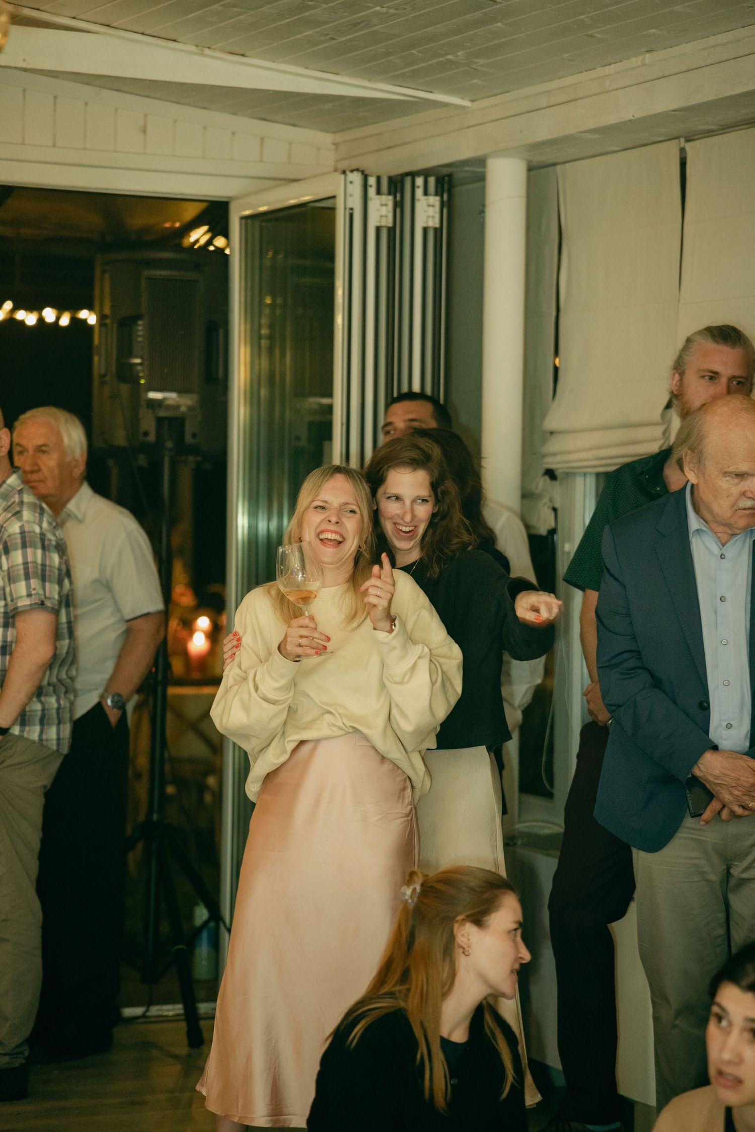 Guests laughing and celebrating at an indoor evening wedding reception party.