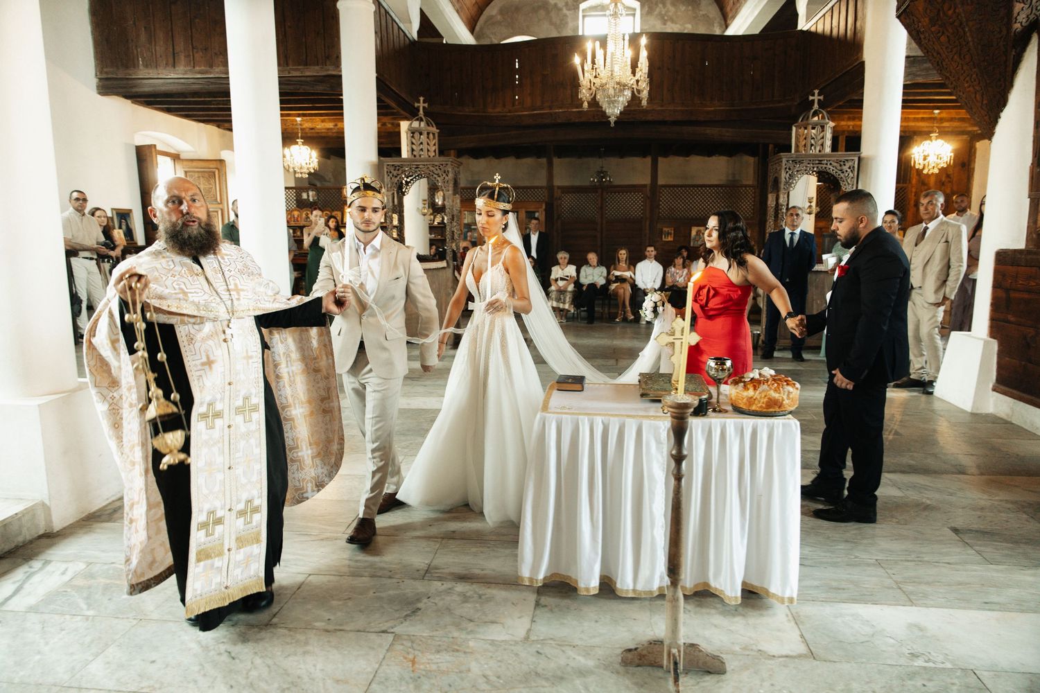 Orthodox priest leads wedding ceremony inside decorated church with bridal party.