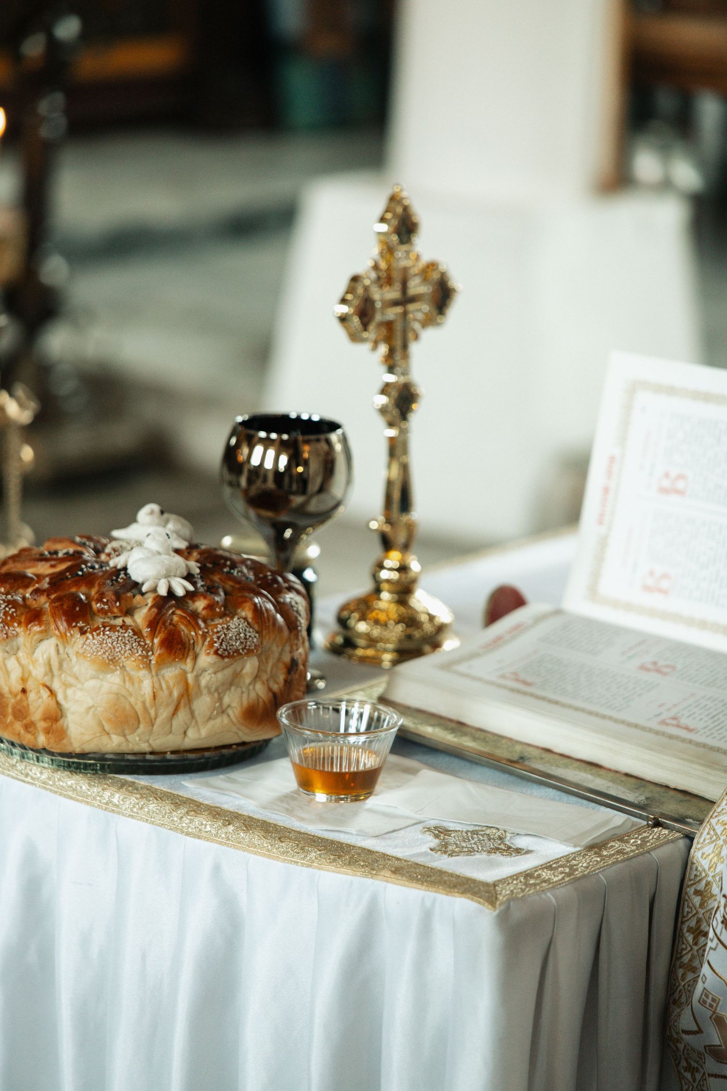 Orthodox wedding ceremony table with braided bread, golden cross, chalice, and open Bible.