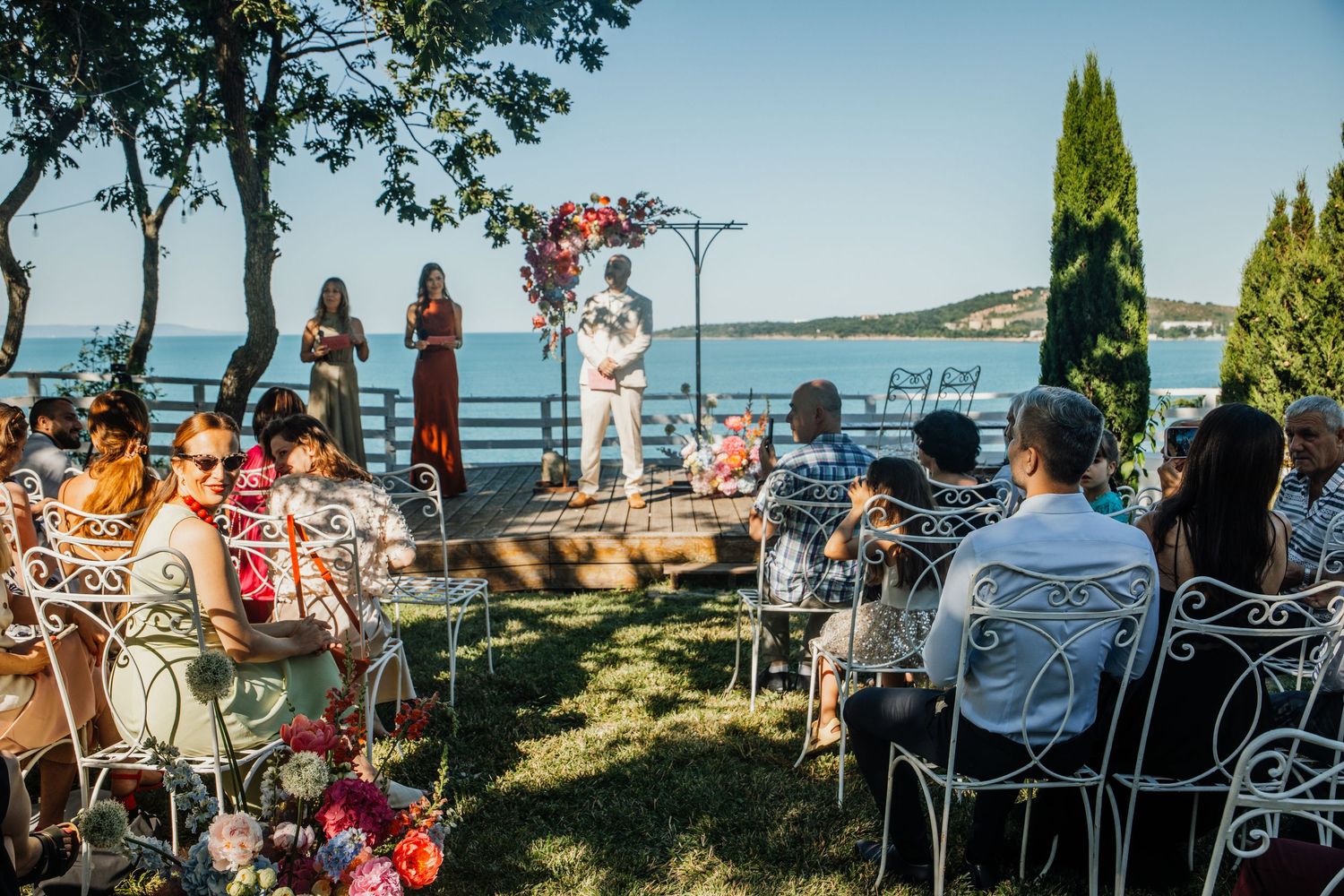 Outdoor wedding ceremony by the lake with guests seated in white chairs facing the altar.