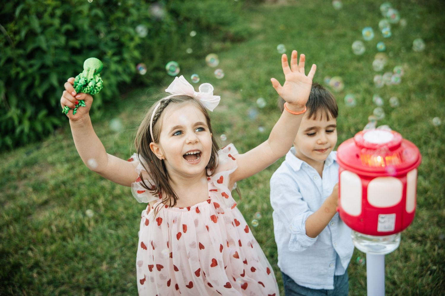 Happy children playing with bubble machine and wands in lush green garden outdoor party.