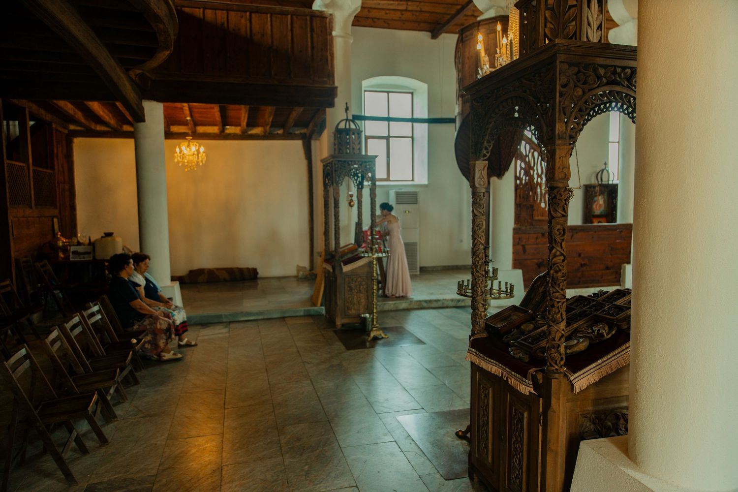 Interior of a traditional Orthodox church with ornate wooden iconostasis and worshippers.