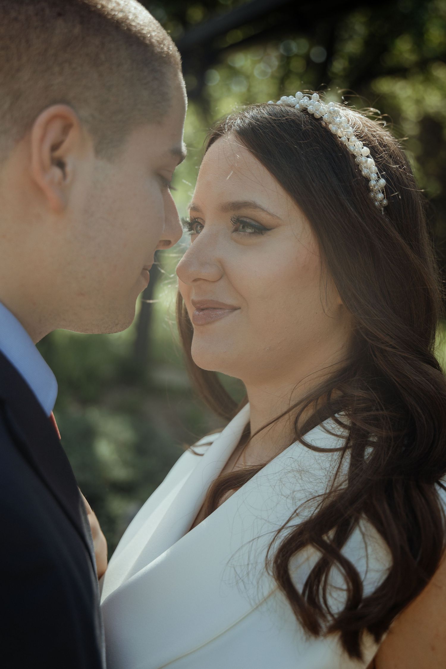 A bride and groom share an intimate moment, the bride wearing a white dress and floral headpiece, gazing lovingly at her groom.