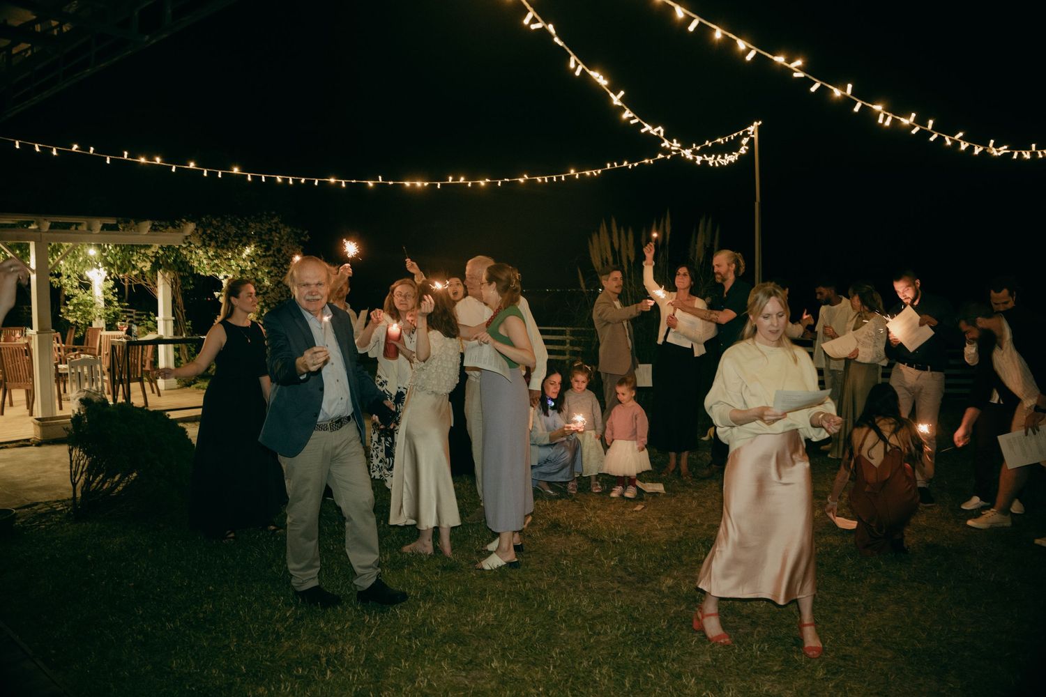 Wedding guests dancing and celebrating under string lights at an outdoor evening garden reception party.