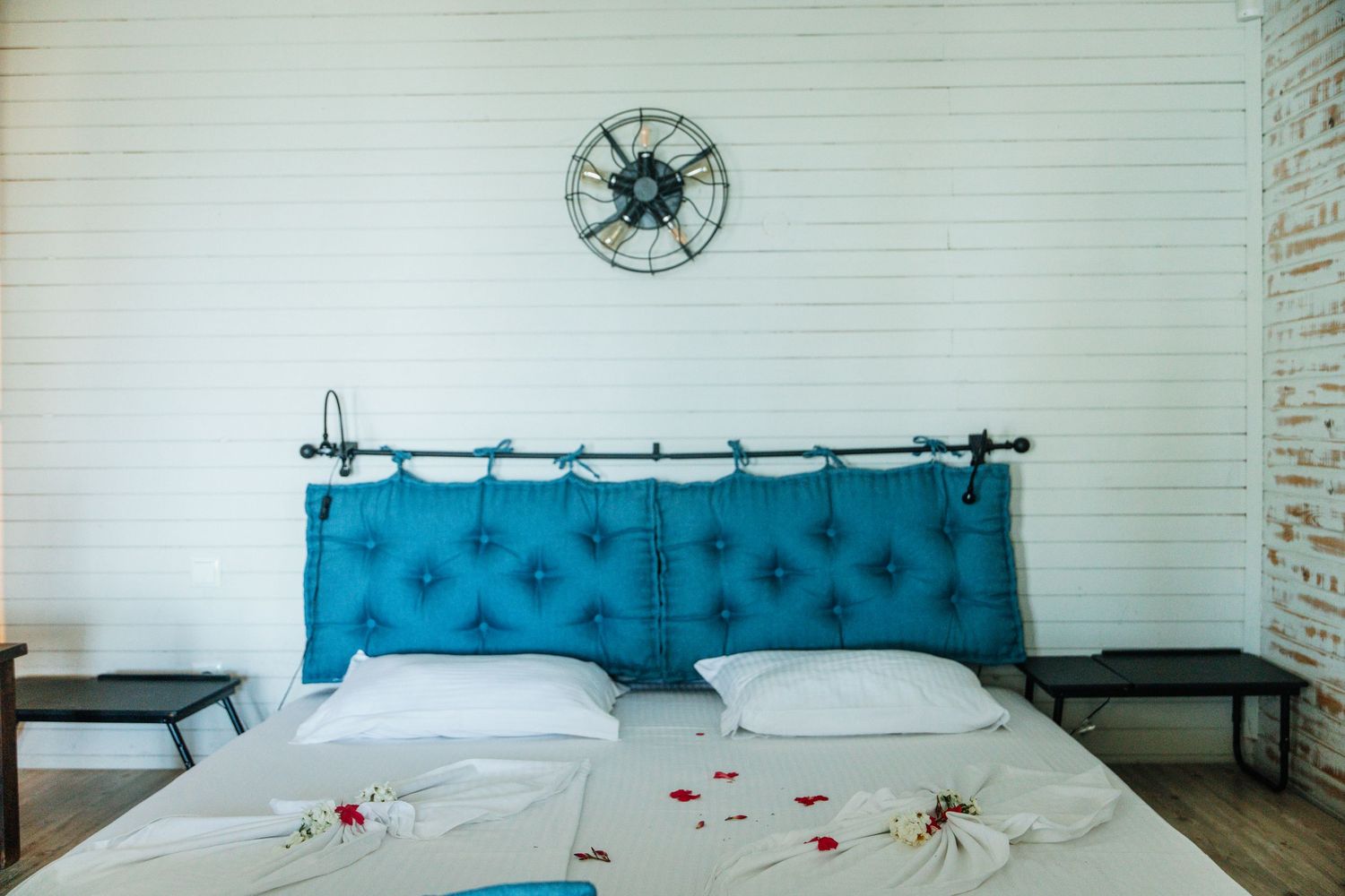 Blue tufted headboard bed with white linens and decorative towel swans in a white brick room.