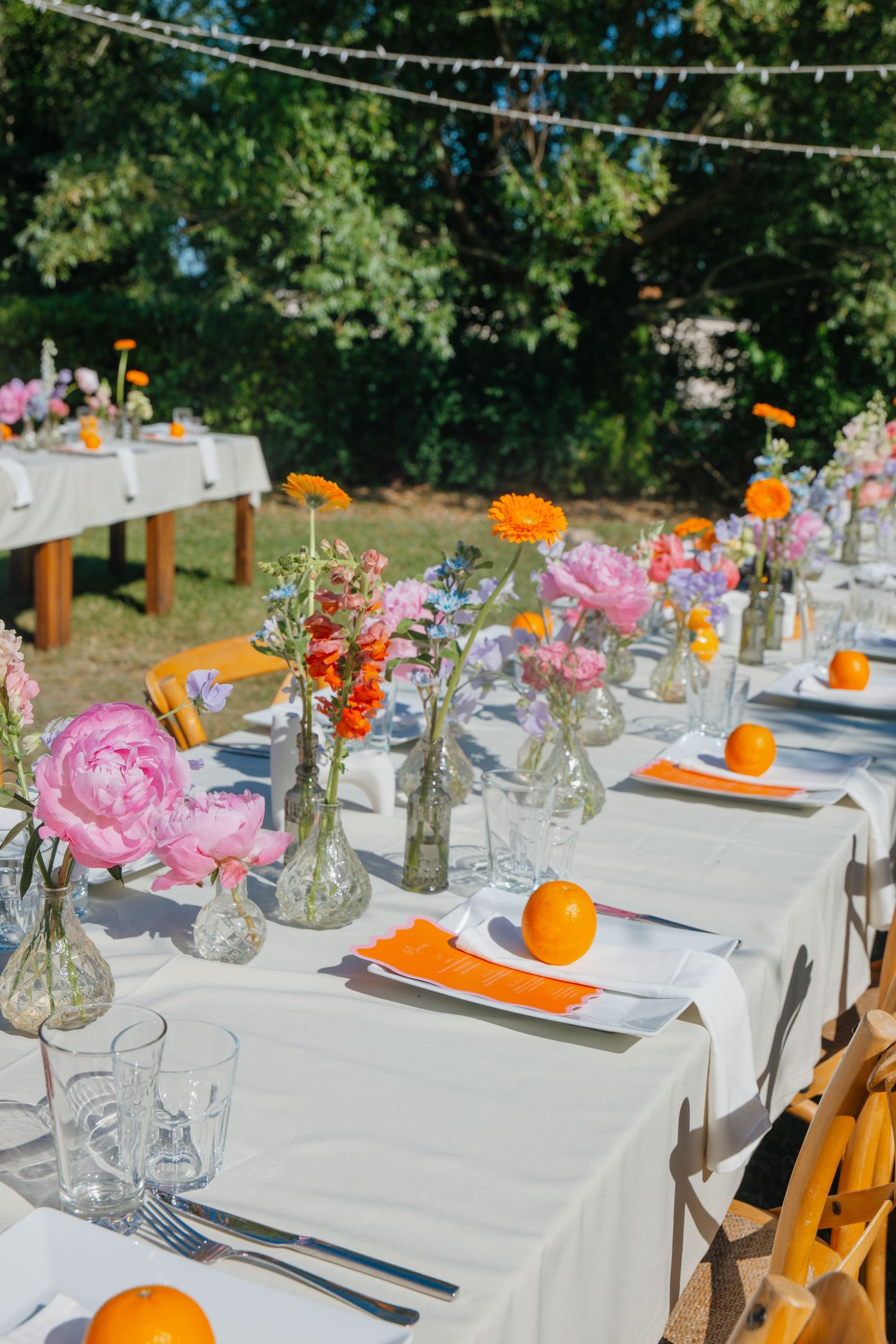 Elegant outdoor wedding reception table with colorful wildflowers, oranges, and white linens.