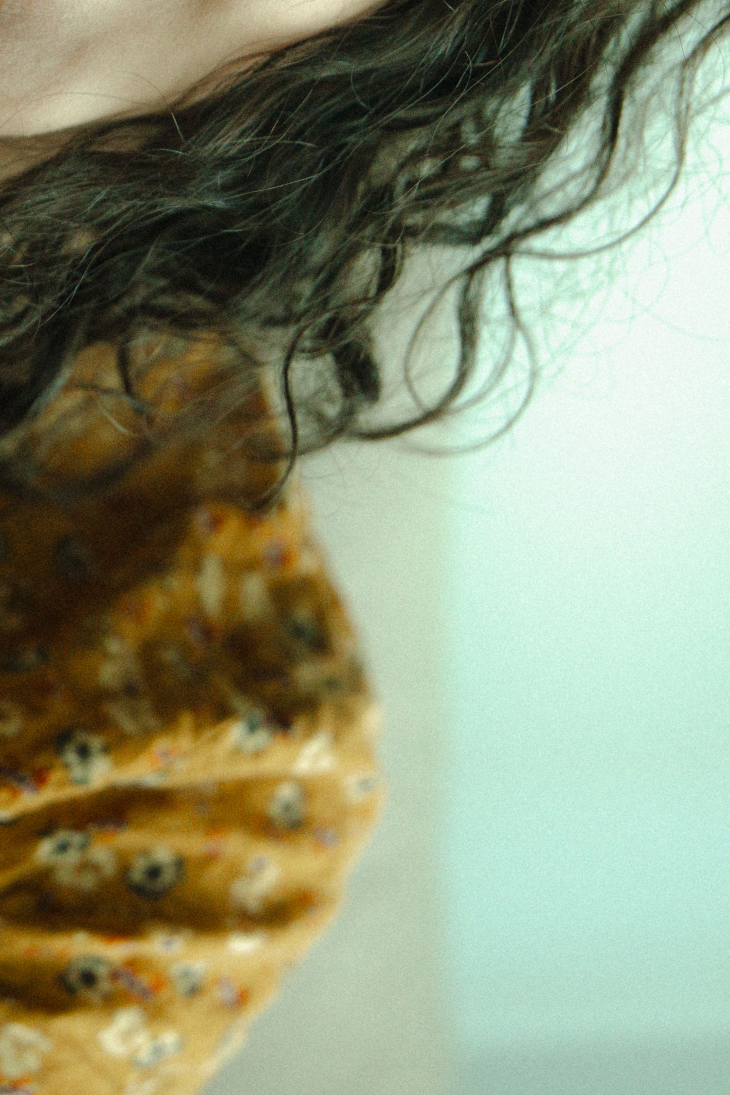 Abstract artistic macro photograph showing dark hair against a blurred orange and teal background with soft focus.